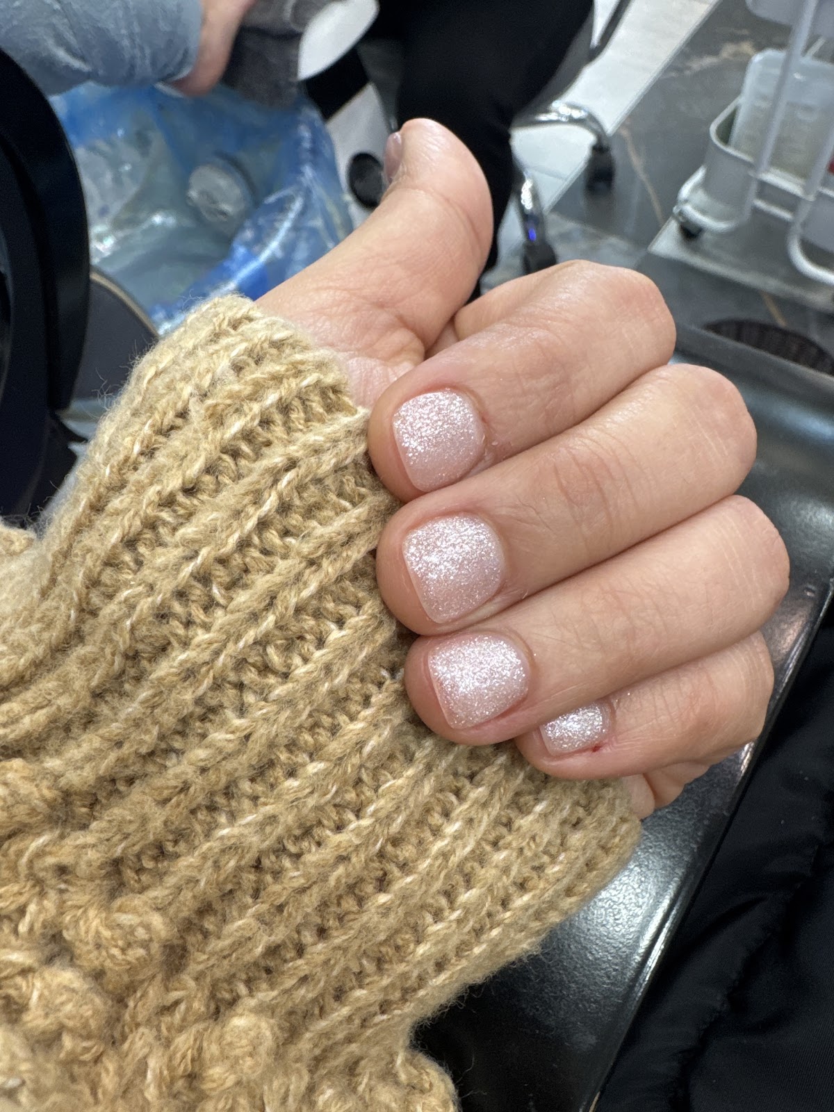 A natural glitter manicure with the Amor Nails and Spa interior visible in the background