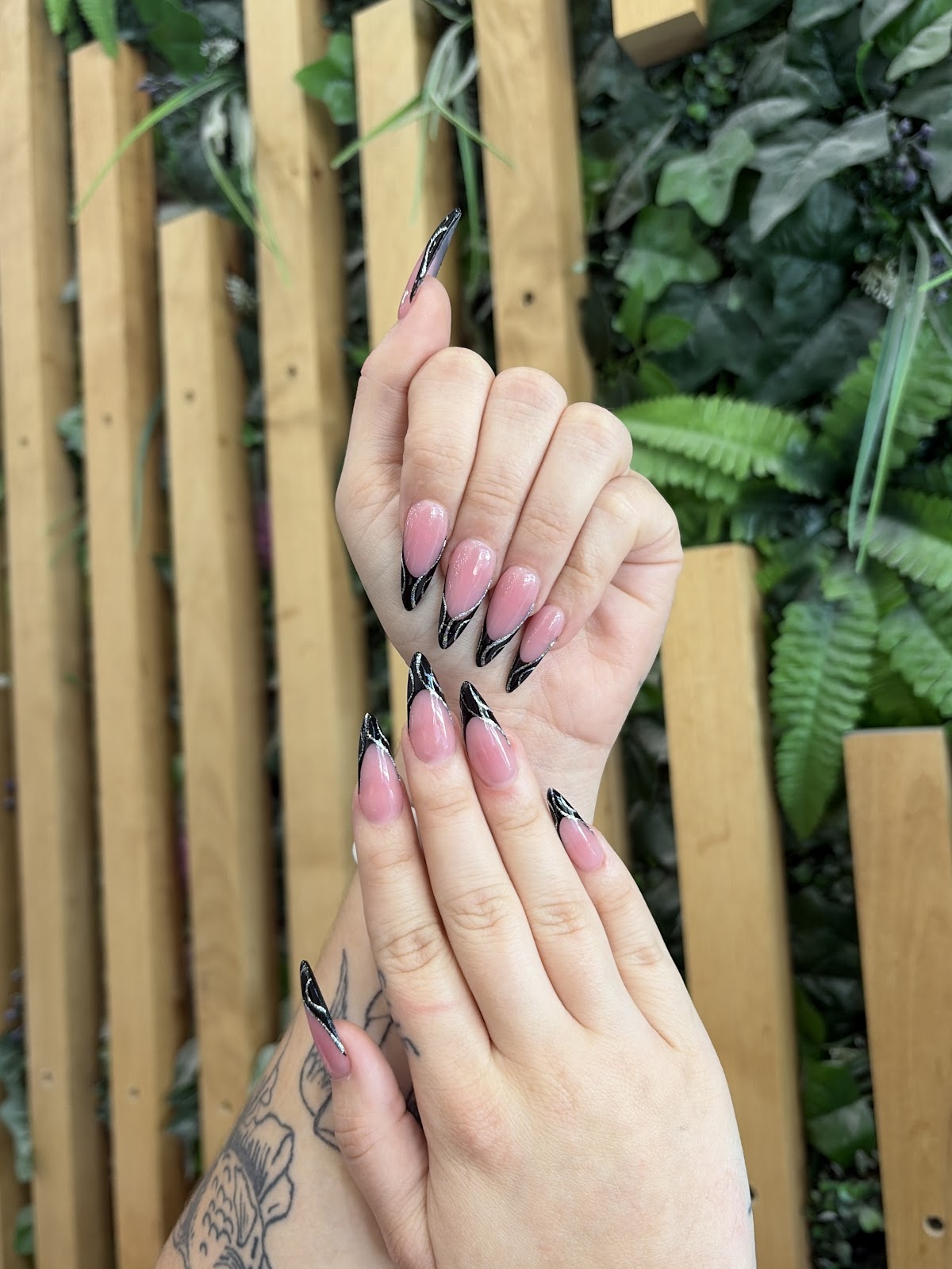 Black and nude French tip stiletto nails against a garden backdrop